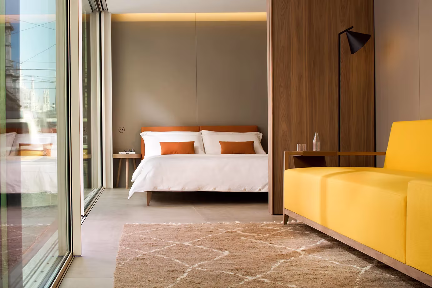 Dormitorio de NO.MADE con cama blanca, panelado de madera y sofá amarillo junto al ventanal corredero