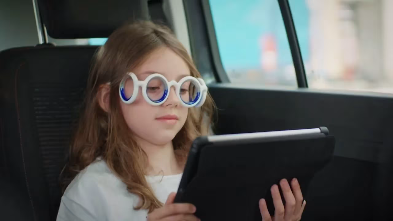 Niña con las gafas antimareo Seetroën de Citroën mirando una tableta en el asiento trasero de un coche