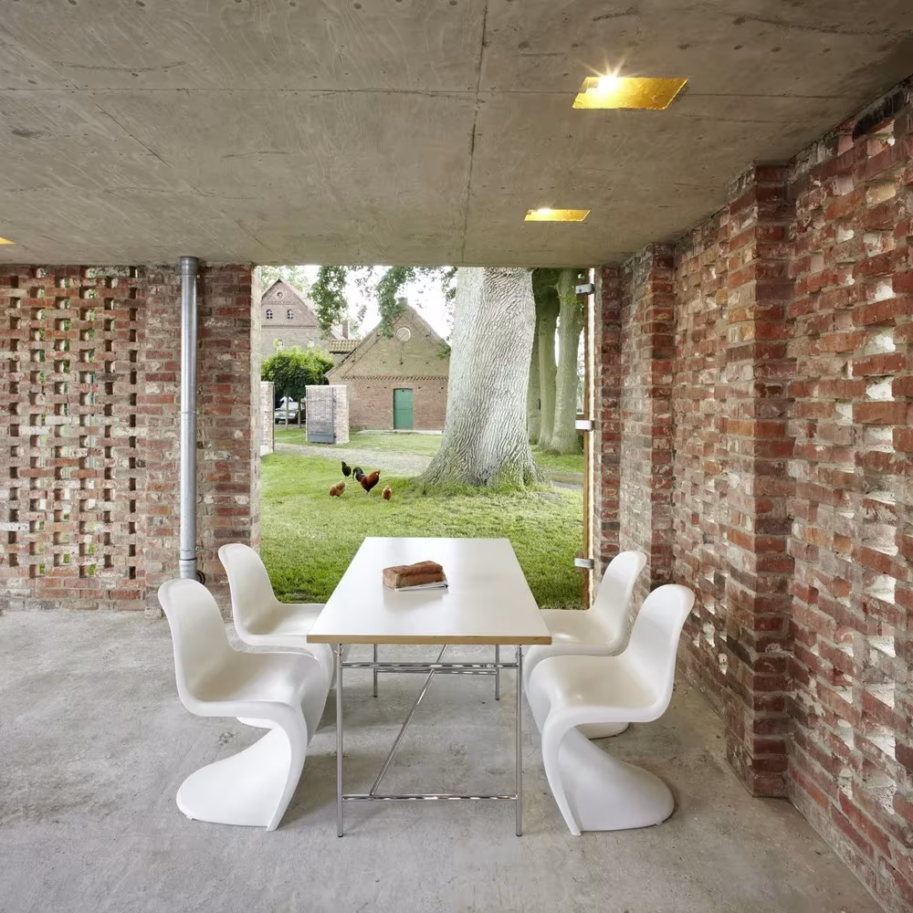 Interior abierto del Remisenpavillon, con muros de ladrillo calado, techo de hormigón y mesa blanca con sillas Panton