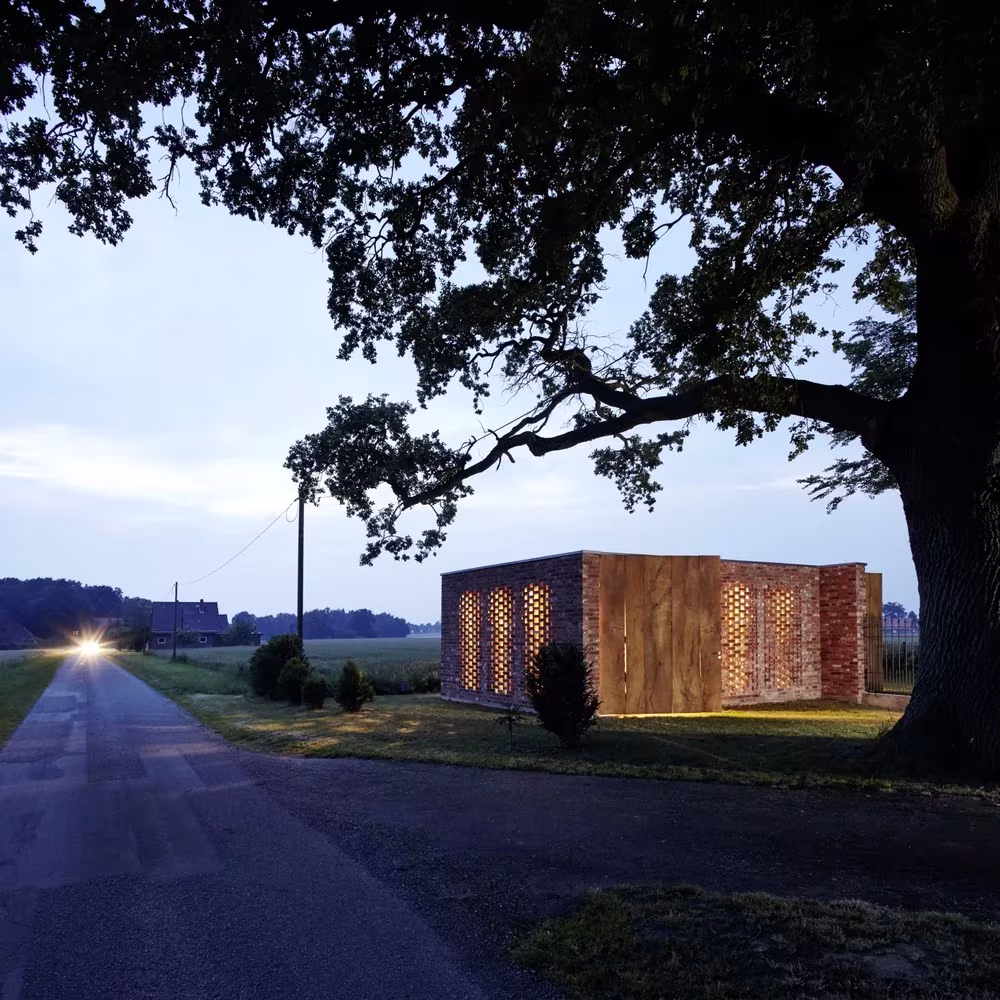 Remisenpavillon al anochecer, con la luz atravesando el ladrillo calado bajo la copa de un roble
