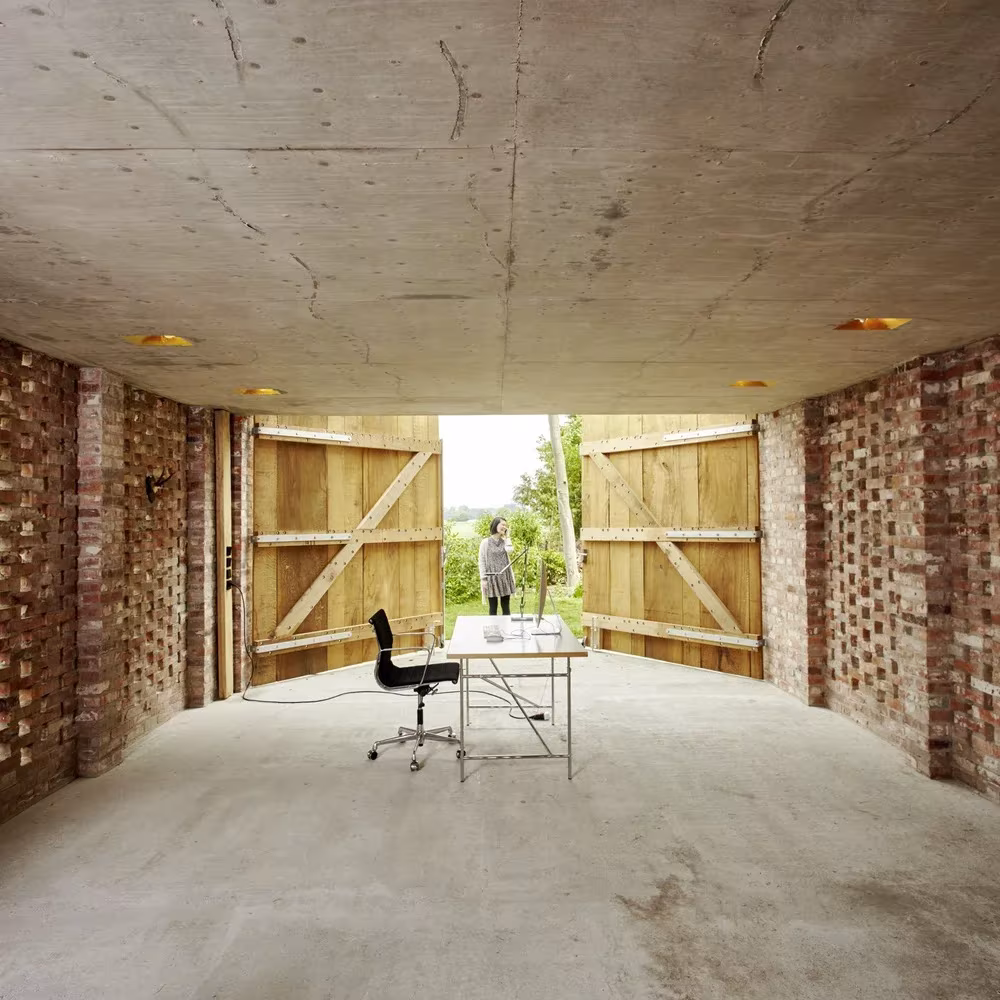 Interior de Remisenpavillon de Wirth Architekten, con muros de ladrillo calado, techo de hormigón y portones de madera