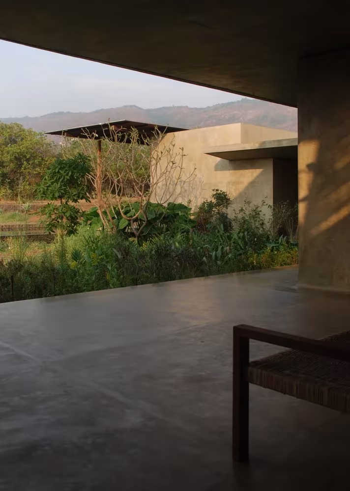 Porche de hormigón de Utsav House abierto al jardín y a un pabellón entre la vegetación, de Studio Mumbai