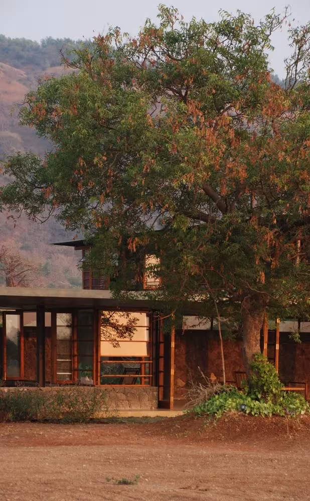 Fachada de carpintería de madera de Utsav House junto a un árbol, con la montaña al fondo, en Maharashtra, India