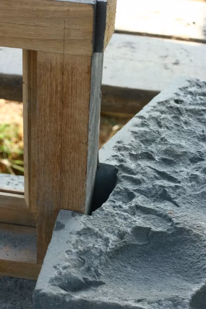 Detalle de un montante de madera sobre un zócalo de basalto de acabado rugoso en Utsav House, Studio Mumbai