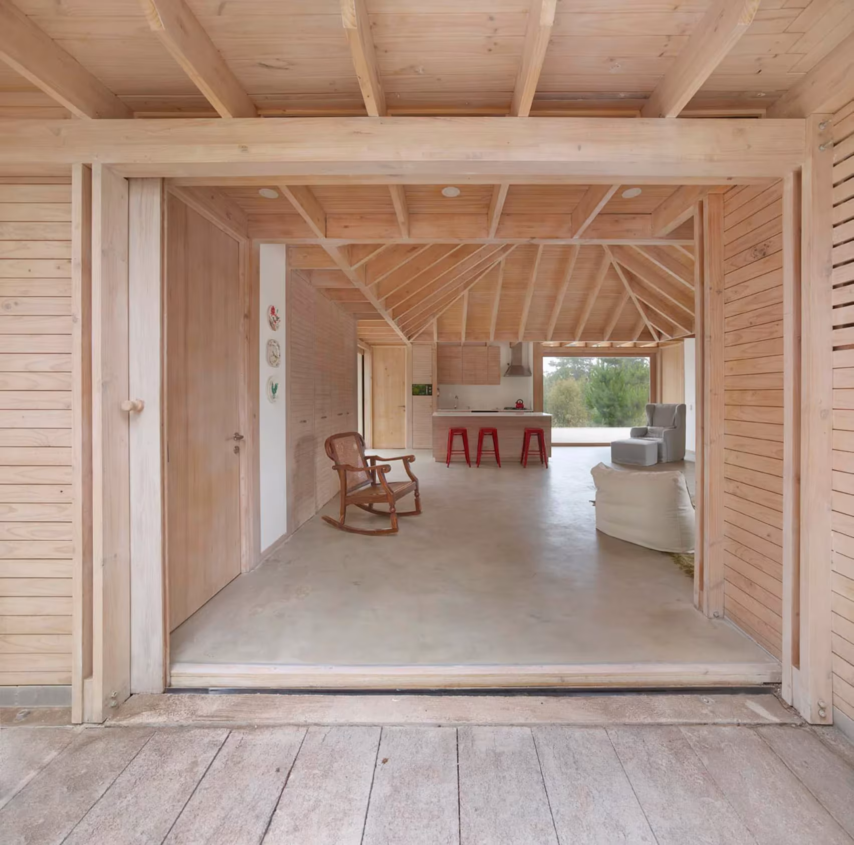 Salón de El Peumo visto desde una galería de madera, con cubierta de vigas y mecedora al fondo, en Chile