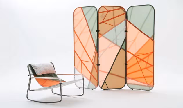 Biombo de tres paneles de paracaídas naranja y verde junto a una mecedora de la colección Canopy de Layer y Raeburn