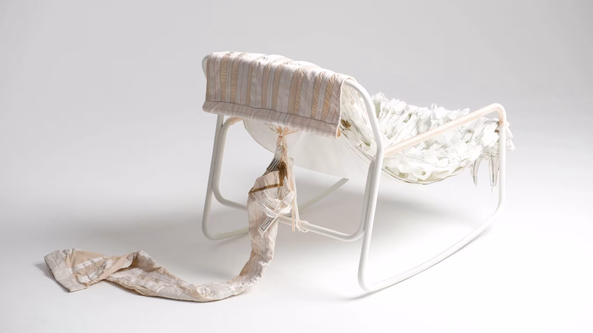 Mecedora blanca de la colección Canopy de Layer y Raeburn con tiras de tela de paracaídas colgando del asiento