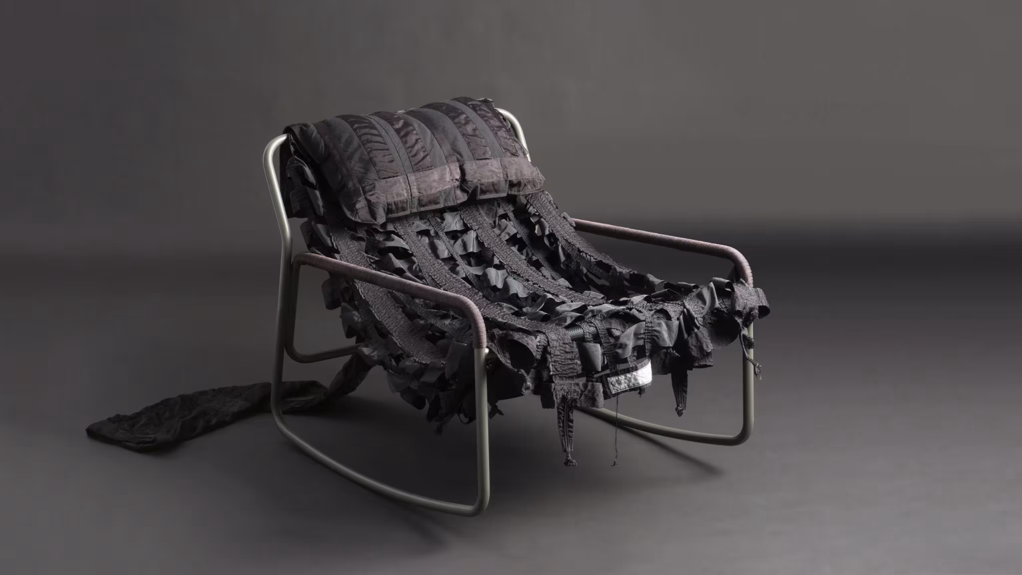 Mecedora Canopy negra de Layer y Raeburn con asiento de tiras de tela de paracaídas sobre fondo oscuro