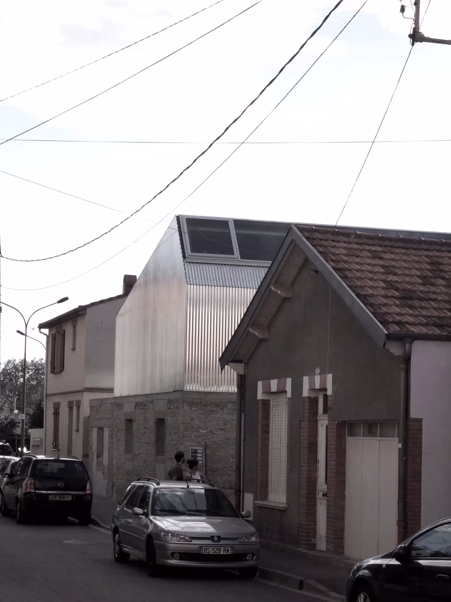Casa M03 de BAST, con su planta superior de acero corrugado asomando sobre una vivienda de ladrillo en una calle francesa