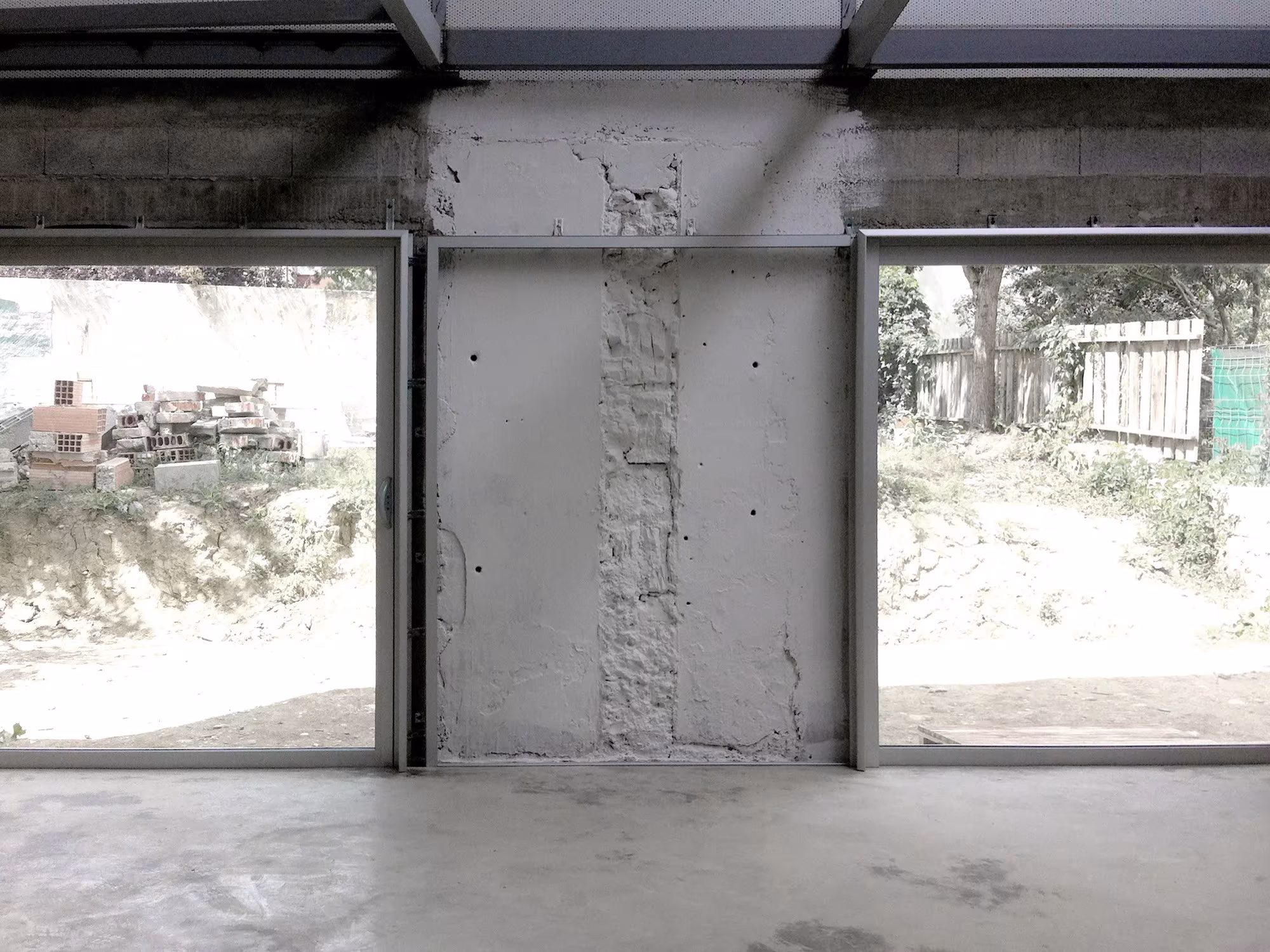 Interior de la planta baja de la Casa M03, con muro de hormigón desgastado y grandes huecos hacia el solar