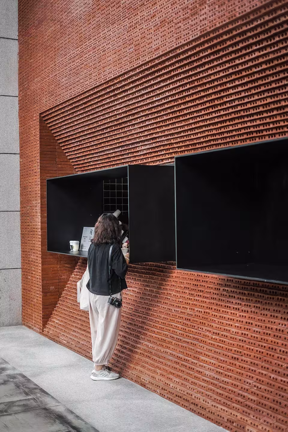 Cliente asomada a una ventanilla de la cafetería de ladrillo de GEOM Design en Guangzhou, con el hueco enmarcado en negro