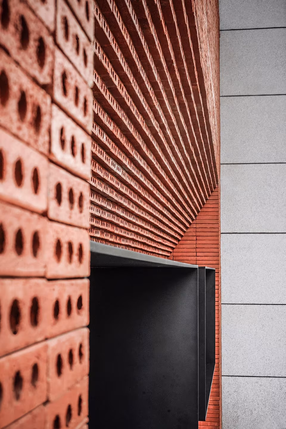 Detalle de ladrillos perforados apilados en la fachada de la cafetería de GEOM Design junto al hueco metálico oscuro