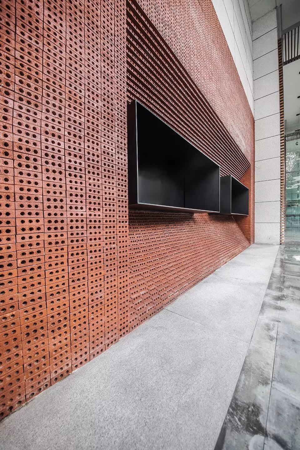 Muro lateral de ladrillo calado de la cafetería de GEOM Design con una ventana negra y el acerado de hormigón