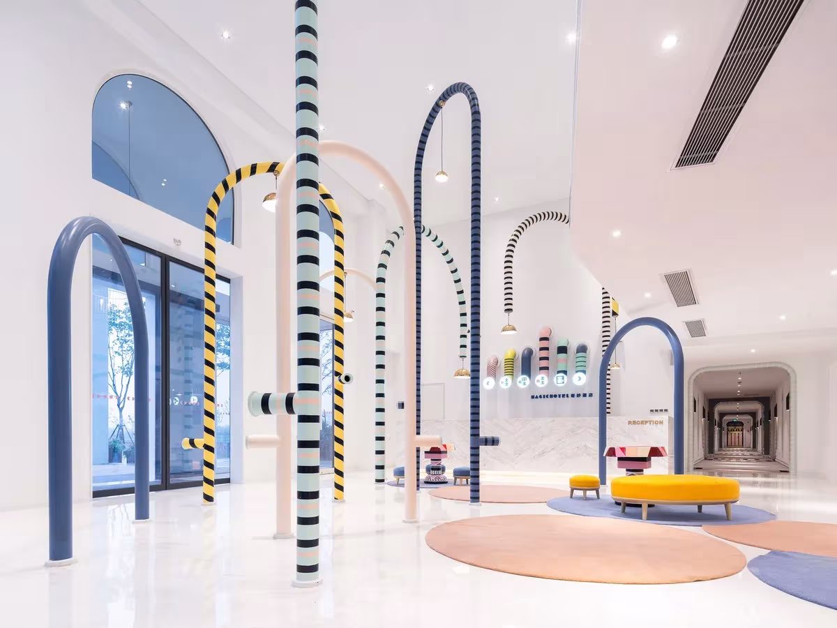 Hall del Magic Hotel de X+Living con arcos de colores, ventanales y un corredor al fondo que lleva a las habitaciones