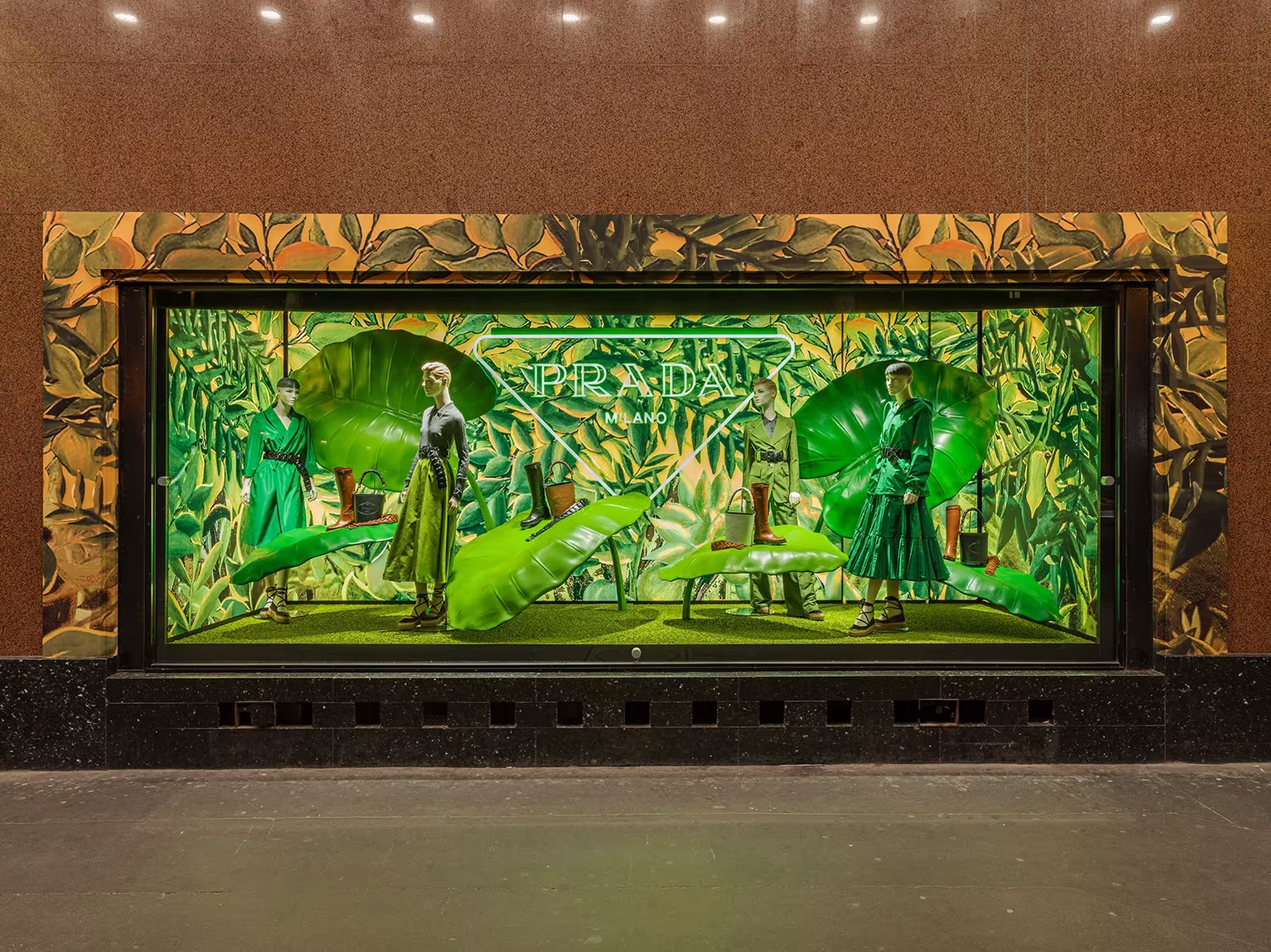 Gran escaparate de Galeries Lafayette con maniquíes y hojas verdes entre un marco de follaje ilustrado, para Prada