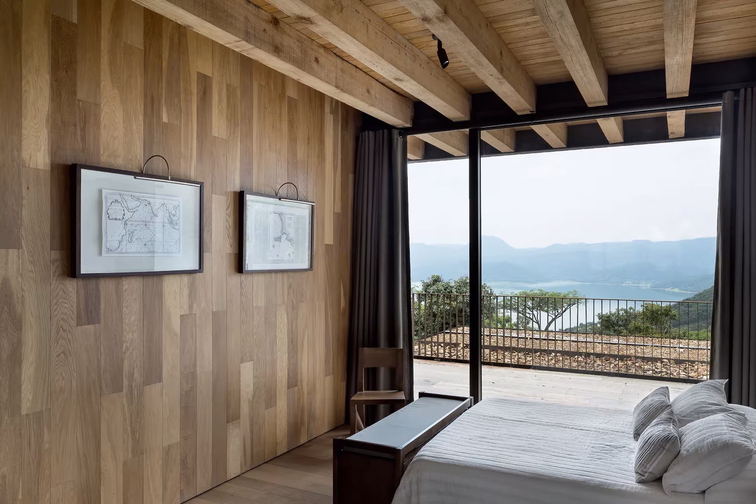 Dormitorio de la Casa Tucán con revestimiento de madera, vigas vistas y un ventanal con vistas al lago Avándaro