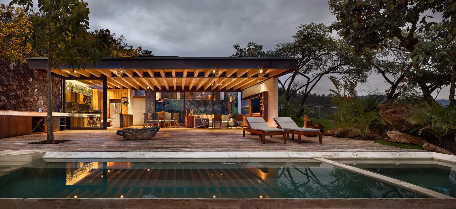 Porche de vigas de madera iluminado al anochecer junto a la piscina de la Casa Tucán, en el Valle de Bravo