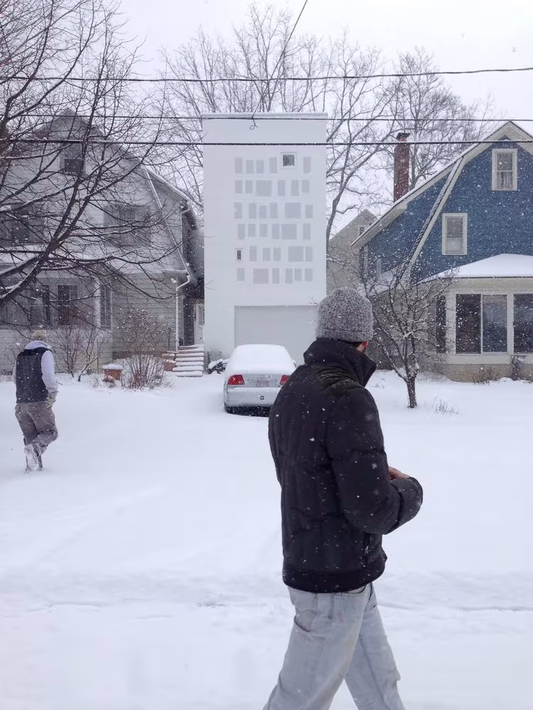 Fachada blanca de Haffenden House en una calle nevada de Syracuse, con un peatón en primer plano