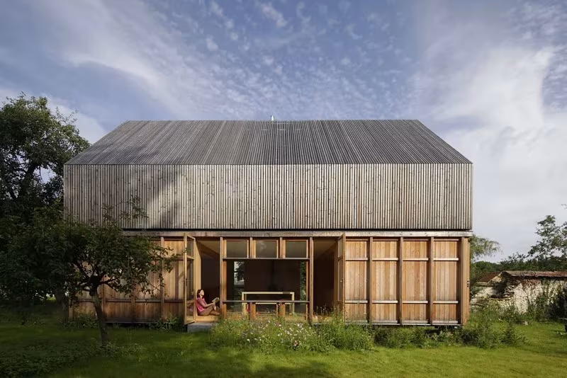 Casa de madera de Arba entre árboles frutales, con cubierta de listones grises y fachada practicable en planta baja