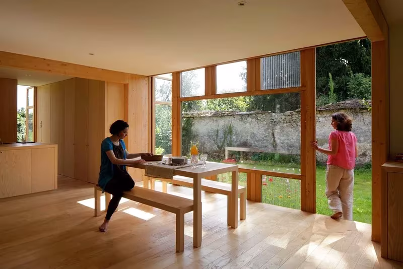 Comedor de madera con una puerta corredera abierta al jardín y al muro de piedra en la Maison dans le Jardin