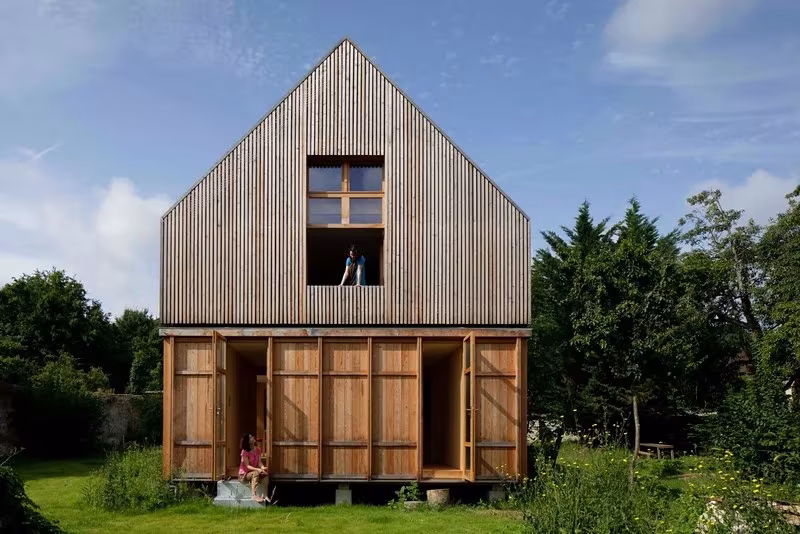Fachada de Maison dans le Jardin con revestimiento de listones de madera, hastial y planta baja con contraventanas abiertas