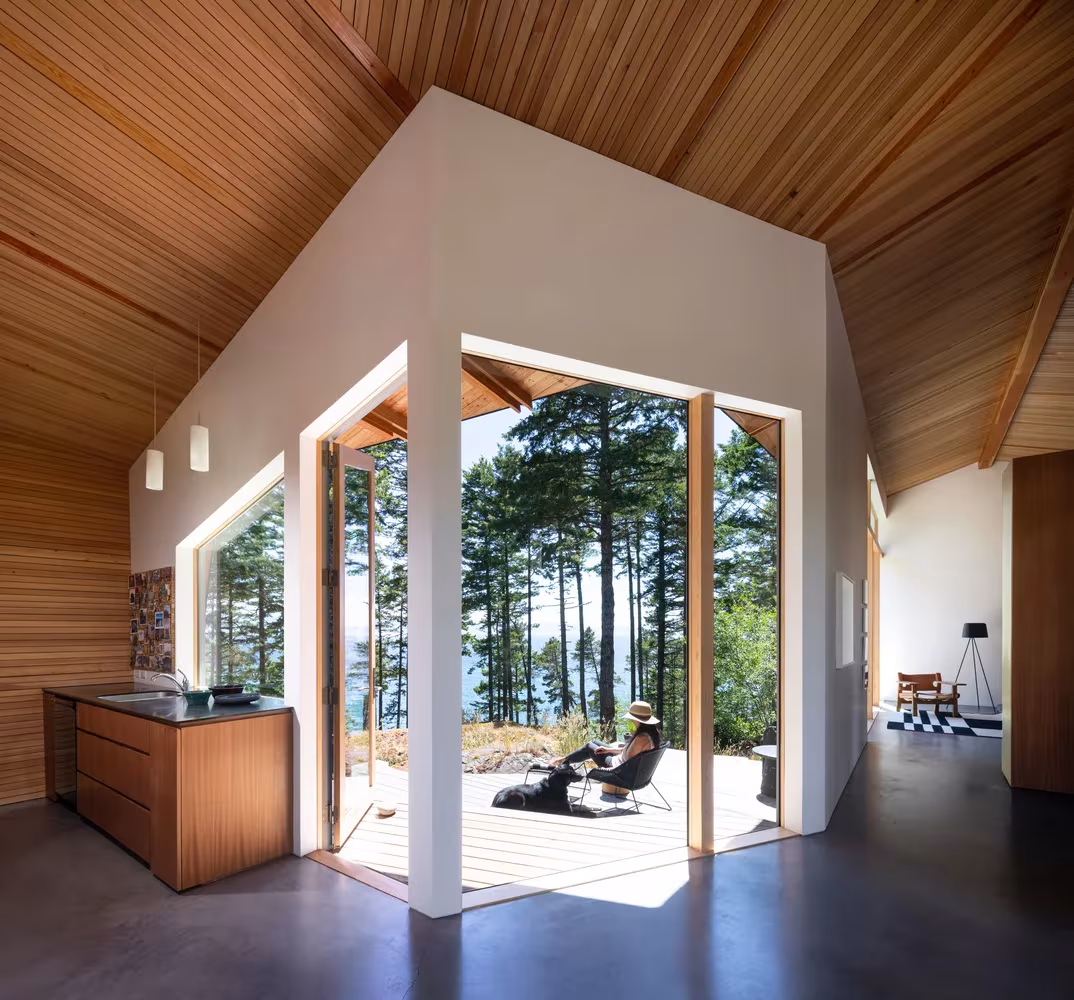Sala de Sooke House con doble altura, techo de cedro inclinado y esquina acristalada abierta al bosque