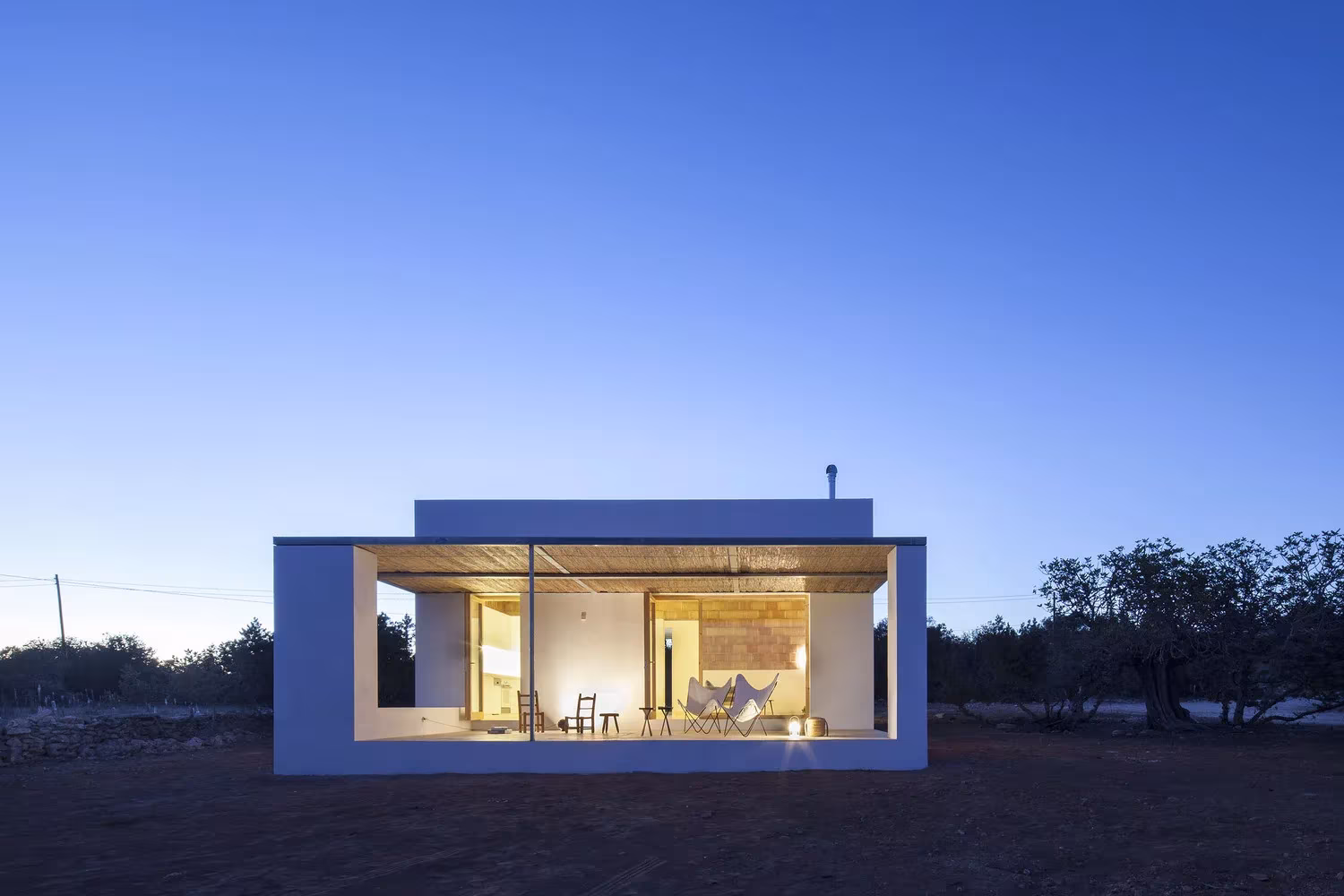 Can Xomeu Rita iluminada al atardecer, con el porche enmarcado en blanco y la sala encendida