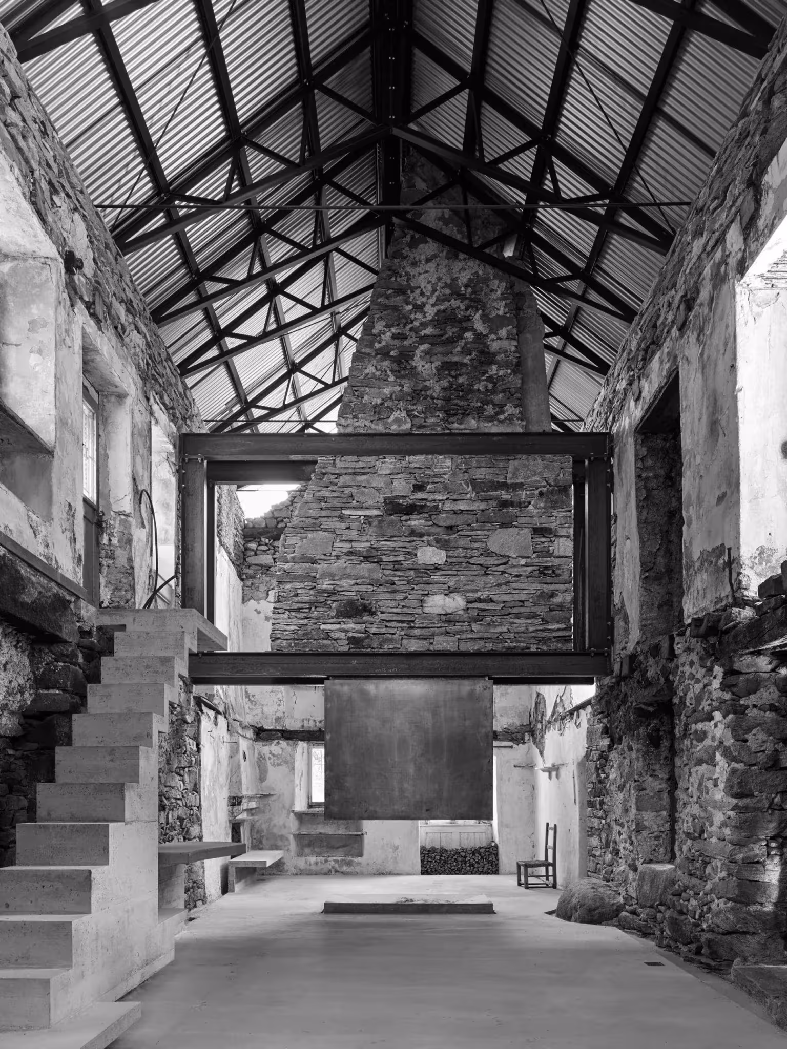 Interior diáfano de Casa Mosogno con estructura de cubierta en acero, escalera de hormigón y chimenea de piedra
