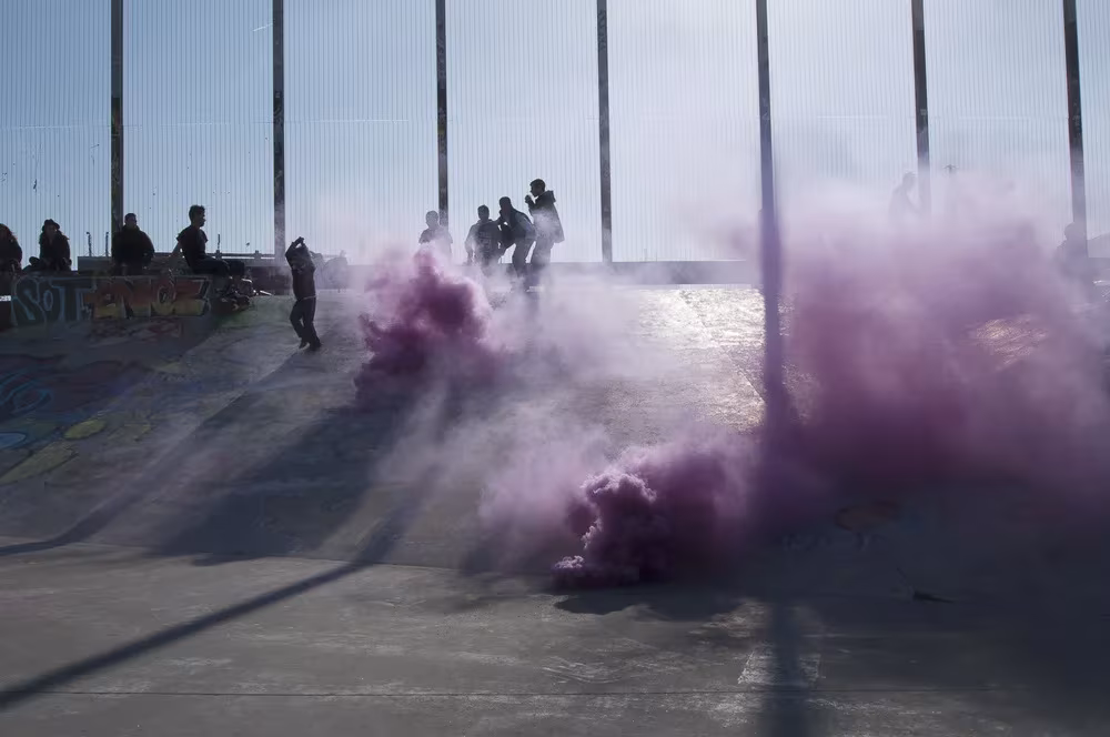 Humo violeta entre un grupo de personas en una pista de cemento, en The Blossom Project