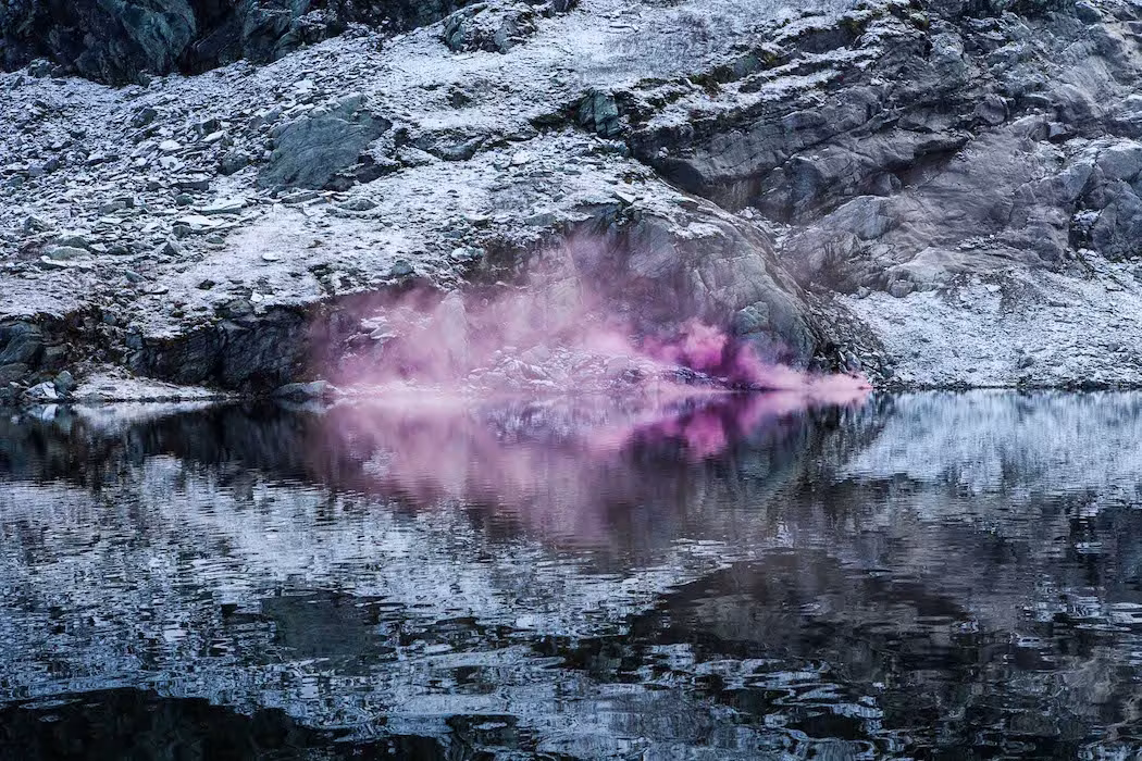 Humo rosa reflejado en una masa de agua entre rocas blanquecinas en The Blossom Project
