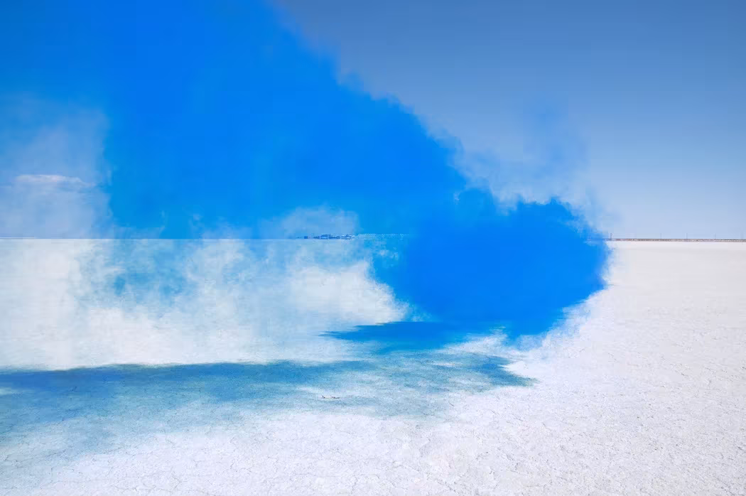 Nube de humo azul intenso sobre una llanura blanca de sal en The Blossom Project