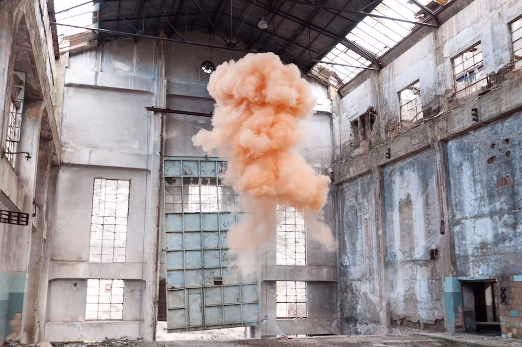 Nube de humo anaranjado dentro de una nave industrial abandonada, en The Blossom Project