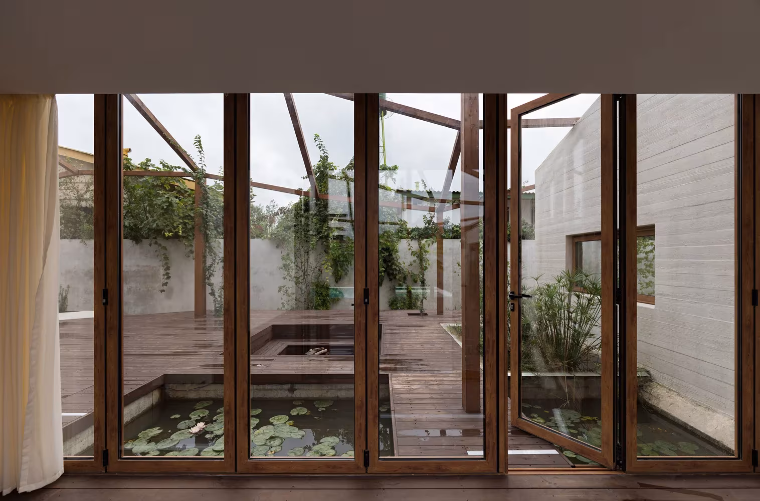 Pasillo acristalado de Villa Vanoosh abierto a un patio con estanque de nenúfares y vegetación