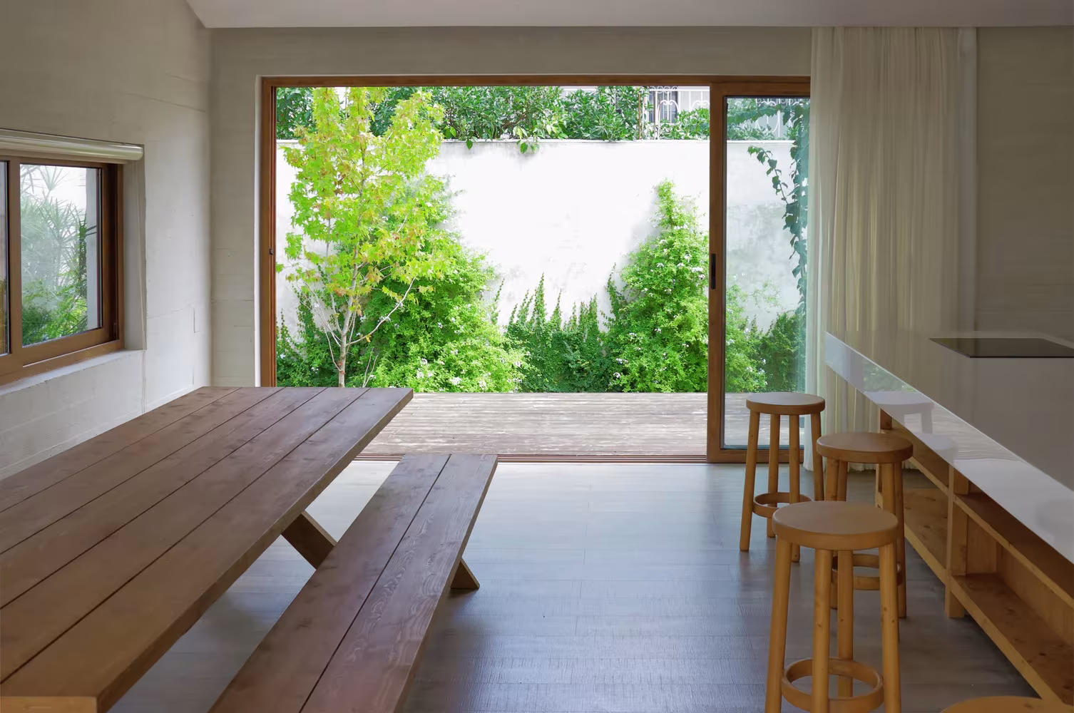 Comedor de Villa Vanoosh con larga mesa de madera, taburetes y un gran ventanal al jardín