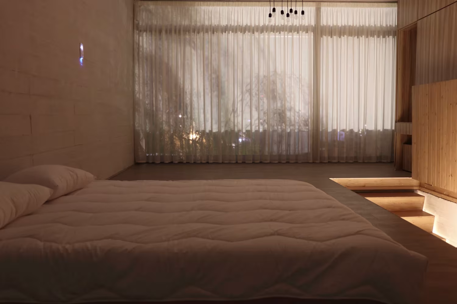 Dormitorio de Villa Vanoosh con cama baja, visillos largos y escalones de madera frente al ventanal