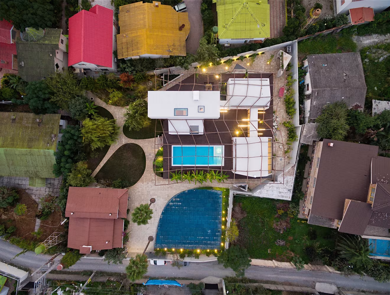 Vista cenital de Villa Vanoosh entre viviendas de cubierta de colores, con la piscina y el entramado de madera