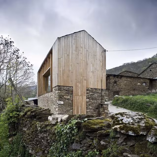 Casa en Paderne con zócalo de piedra y volumen superior de madera entre construcciones tradicionales de Lugo