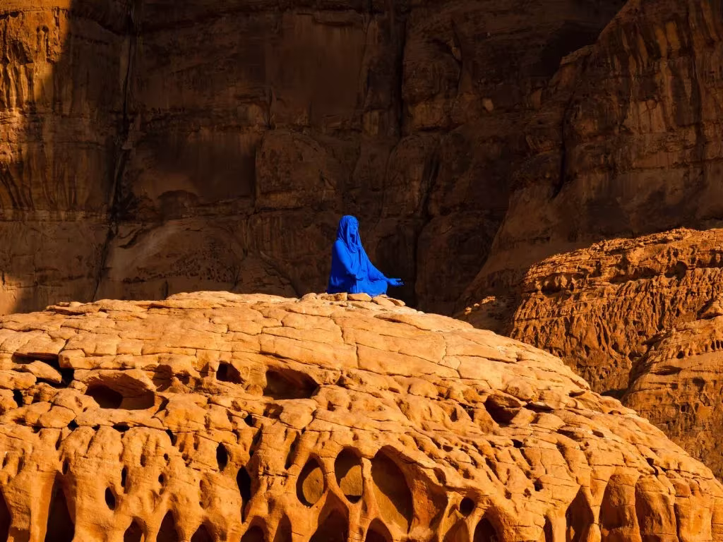 Figura azul sentada sobre la roca de arenisca erosionada de AlUla durante Desert X, Arabia Saudita