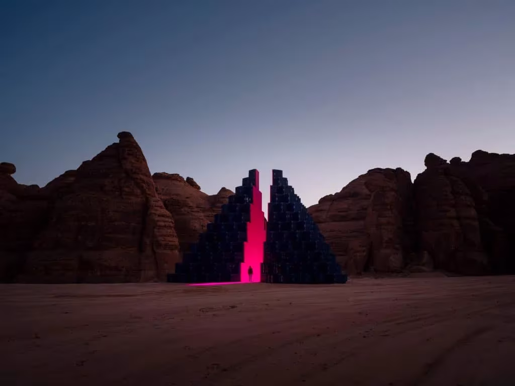 Instalación piramidal escalonada con una grieta rosa iluminada entre las formaciones rocosas de AlUla, Desert X
