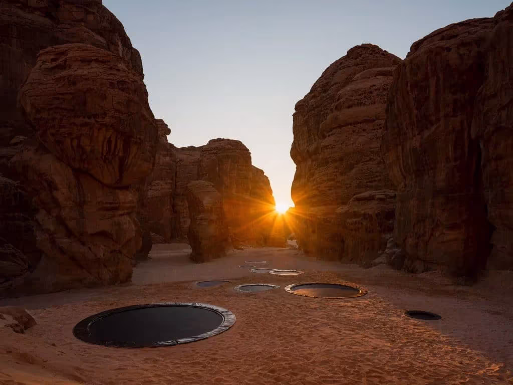 Círculos oscuros hundidos en el suelo de un cañón de AlUla con el sol entre las rocas, instalación de Desert X