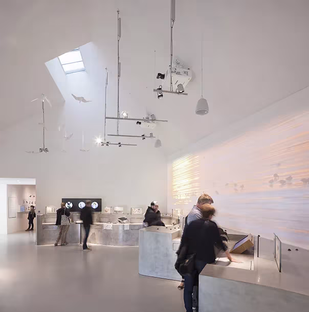 Visitantes ante las vitrinas y los móviles colgantes de la exposición del centro del Mar de Wadden de Dorte Mandrup