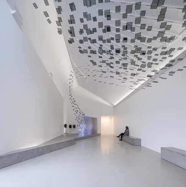 Sala expositiva blanca del Mar de Wadden con techo inclinado de paneles colgantes y un banco de hormigón