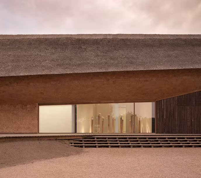 Entrada del centro de Dorte Mandrup bajo el faldón de paja, con escalones de madera y una sala iluminada