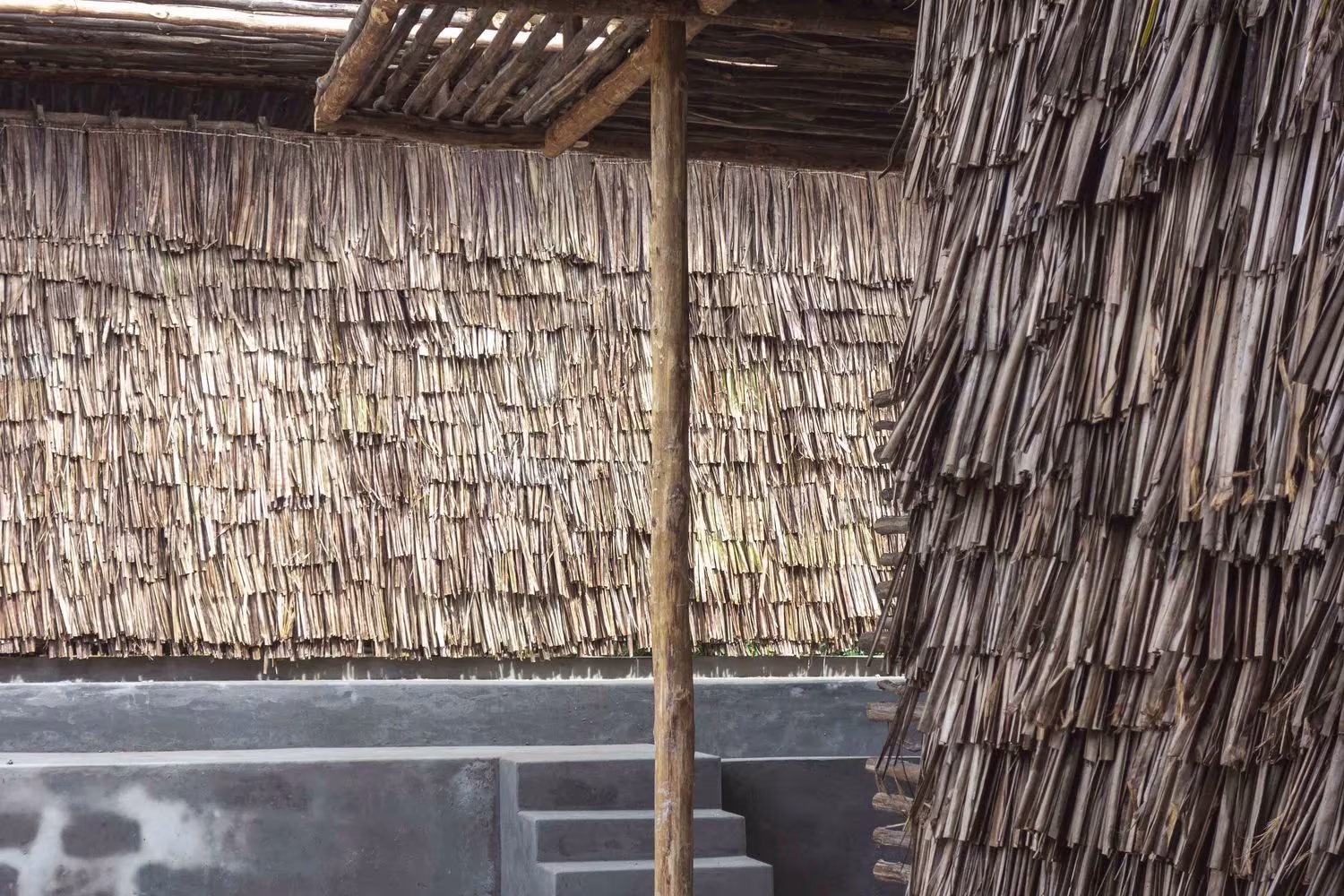 Detalle de las hojas de coco superpuestas y un poste de madera en el cerramiento del Eco Moyo, de Architectopia