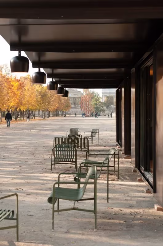 Soportal del Kiosque con lámparas colgadas y sillas verdes de jardín junto a la alameda de las Tullerías