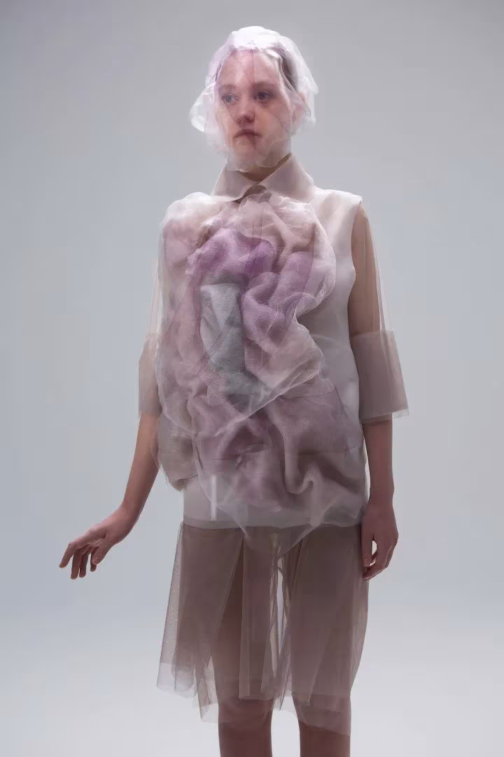 Modelo con vestido de capas translúcidas de organza violeta y capucha transparente, de Ying Gao
