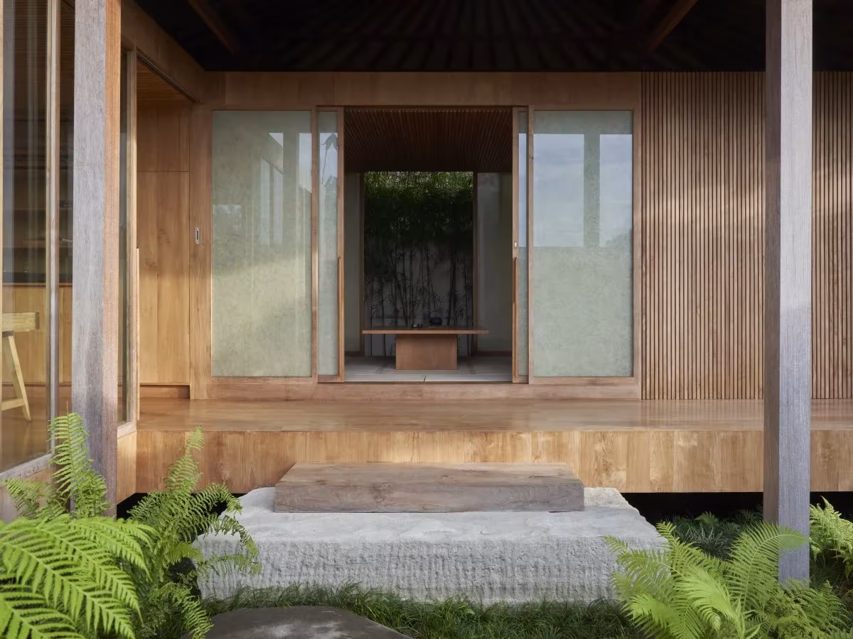 Pabellón de madera de HER abierto a un jardín de helechos, con puertas correderas y escalón de piedra