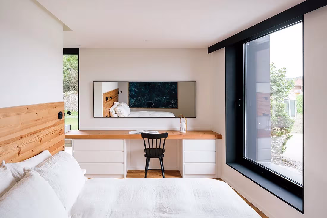 Dormitorio con revestimiento de madera, escritorio blanco y gran ventana de marco negro en la casa de Güemes