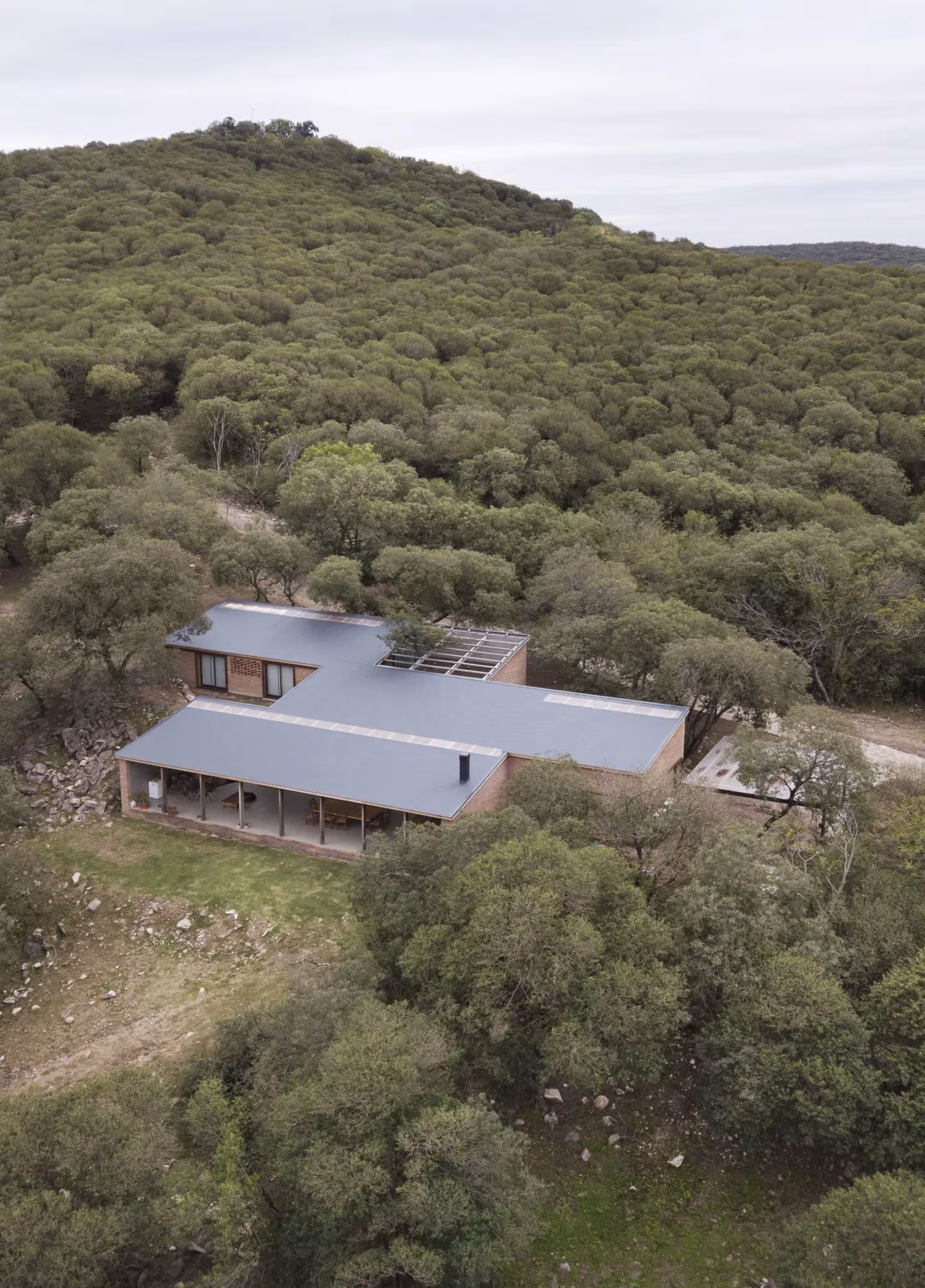 Vista aérea de la Casa JB con cubierta metálica sobre una ladera boscosa de las sierras de Córdoba