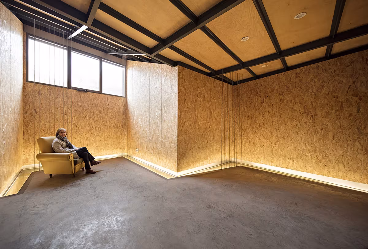 Sala de paredes de OSB y techo de vigas metálicas con luz indirecta en el zócalo, en Casa Piedrabuena